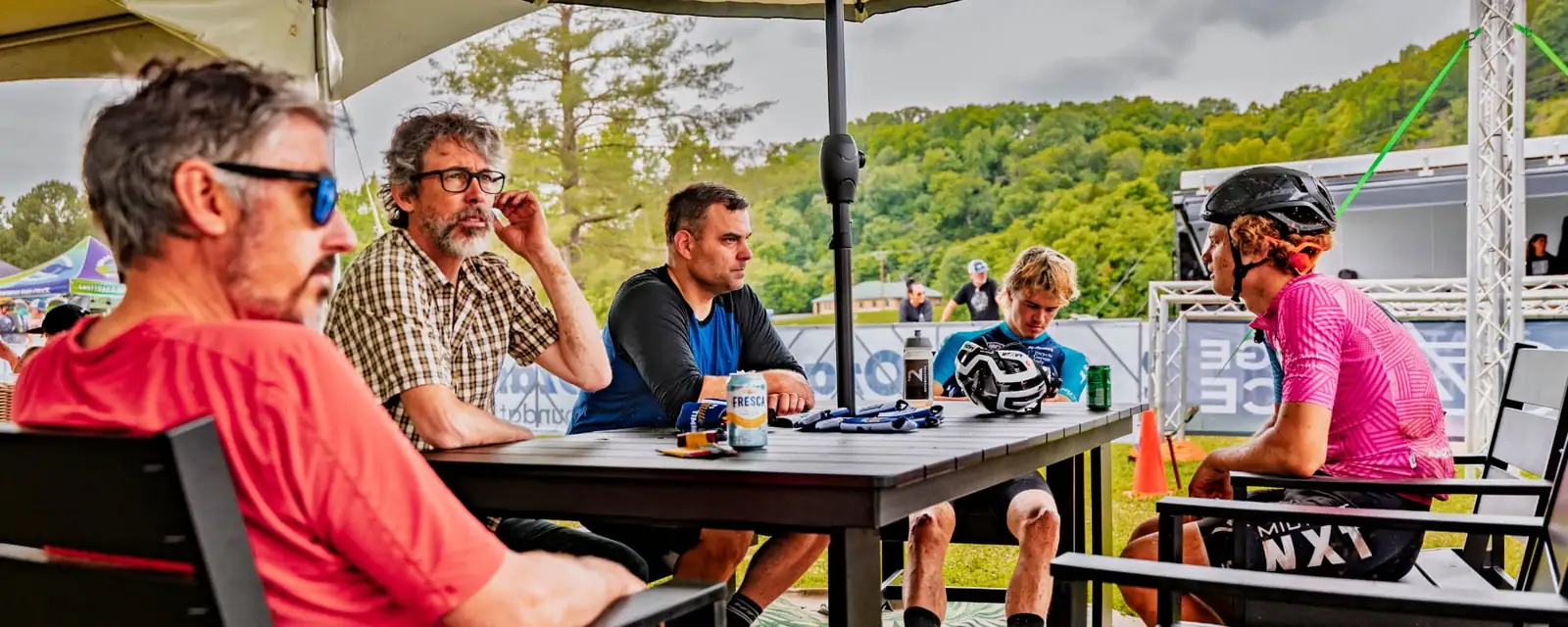Racers and crew talking around a table under a canopy at the Oz Stage Race venue